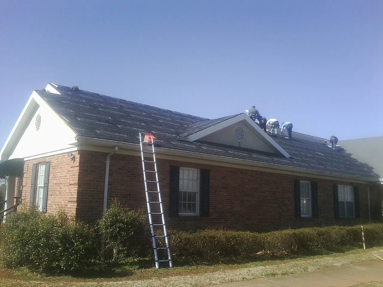 Crew tearing shingles off a brick ranch roof with a ladder set — Emergency Roof Repair work by our crew in Agoura Hills
