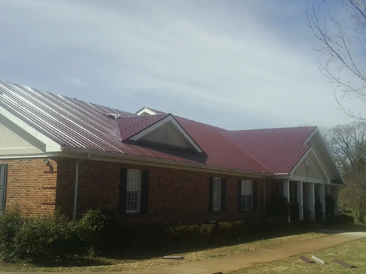 Red metal roof with gabled entries on a long brick building, from a Hail Damage Roof Repair job in Agoura Hills
