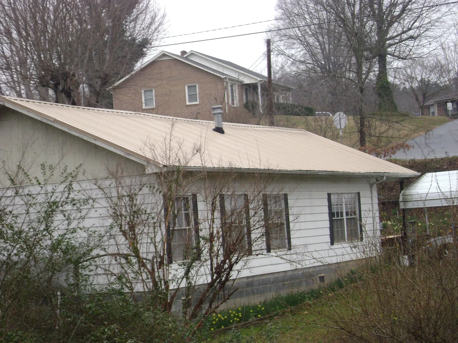 Tan metal roof on a white sided house set into a hillside — Commercial Roofing by Roofing Brothers in Agoura Hills